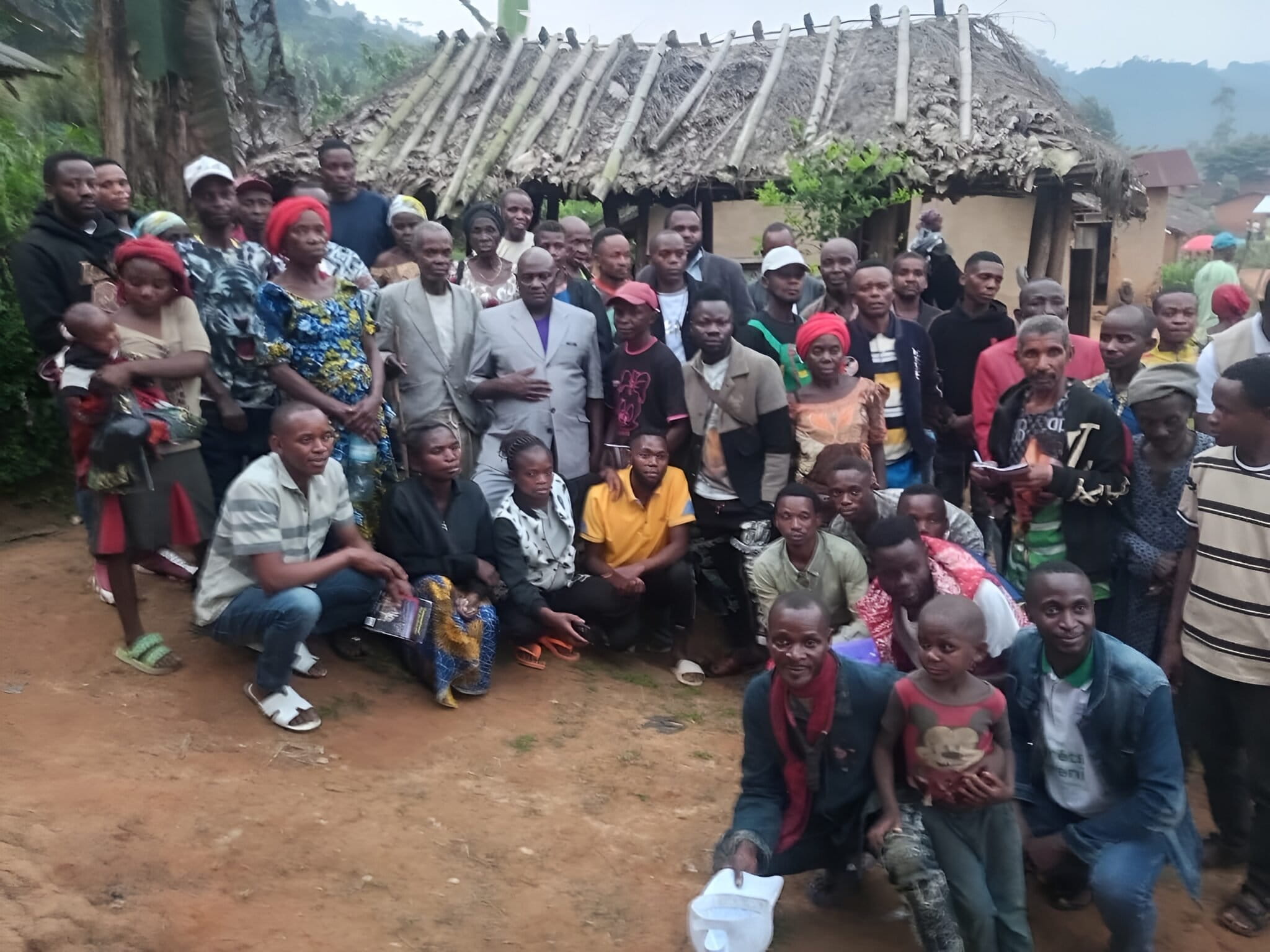Gangala Yafali Mangusa Jr. en leden van de Bamasobha-gemeenschap poseren voor een familiefoto na een gemeenschapsbijeenkomst over sociale cohesie binnen de Local Community Forest Concession (CFCL). Afbeelding door Jéremie Kyaswekera Kakule.