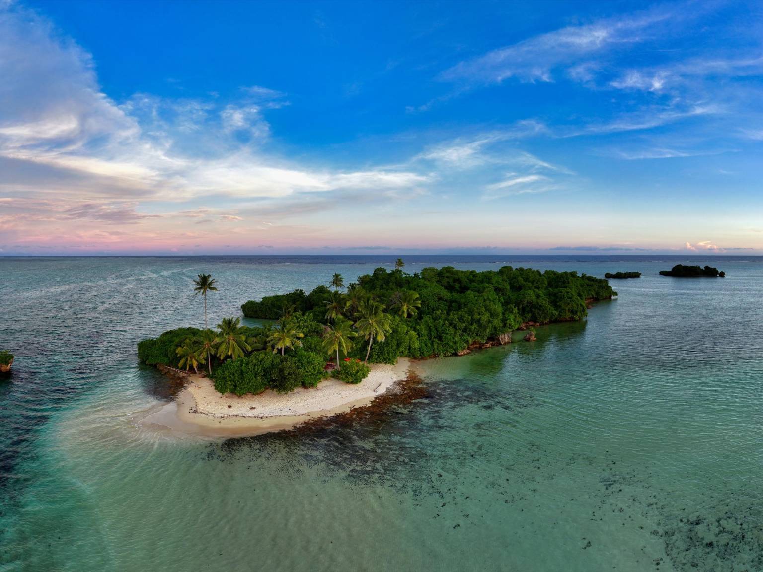 Luchtfoto van een eiland in Fiji bedekt met bomen tegen de blauwe en roze lucht.