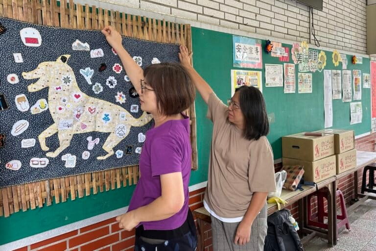Siraya-taaldocenten Silia Pan, links, en Uma Talavan hangen een wandtapijt op, gemaakt door studenten van de Koupi Experimental Elementary School in Tainan, Taiwan, op 21 augustus 2026. Afbeelding door Aylin Ho voor Mongabay.