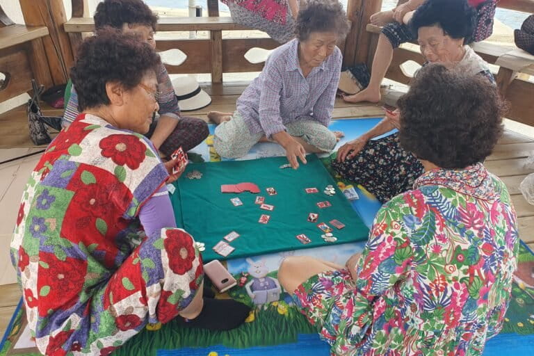 Een groep haenyeo, waaronder van links met de klok mee, Im Gil-seok, Kim Choon-hee en Lee Yeon-oak Haenyeo spelen go-stop, een oud Koreaans kaartspel, in een prieel aan de kust in Guman-ri, Zuid-Korea, op 15 augustus 2026, tijdens hun wekelijkse bijeenkomst. Afbeelding door Andrew Jeong voor Mongabay.