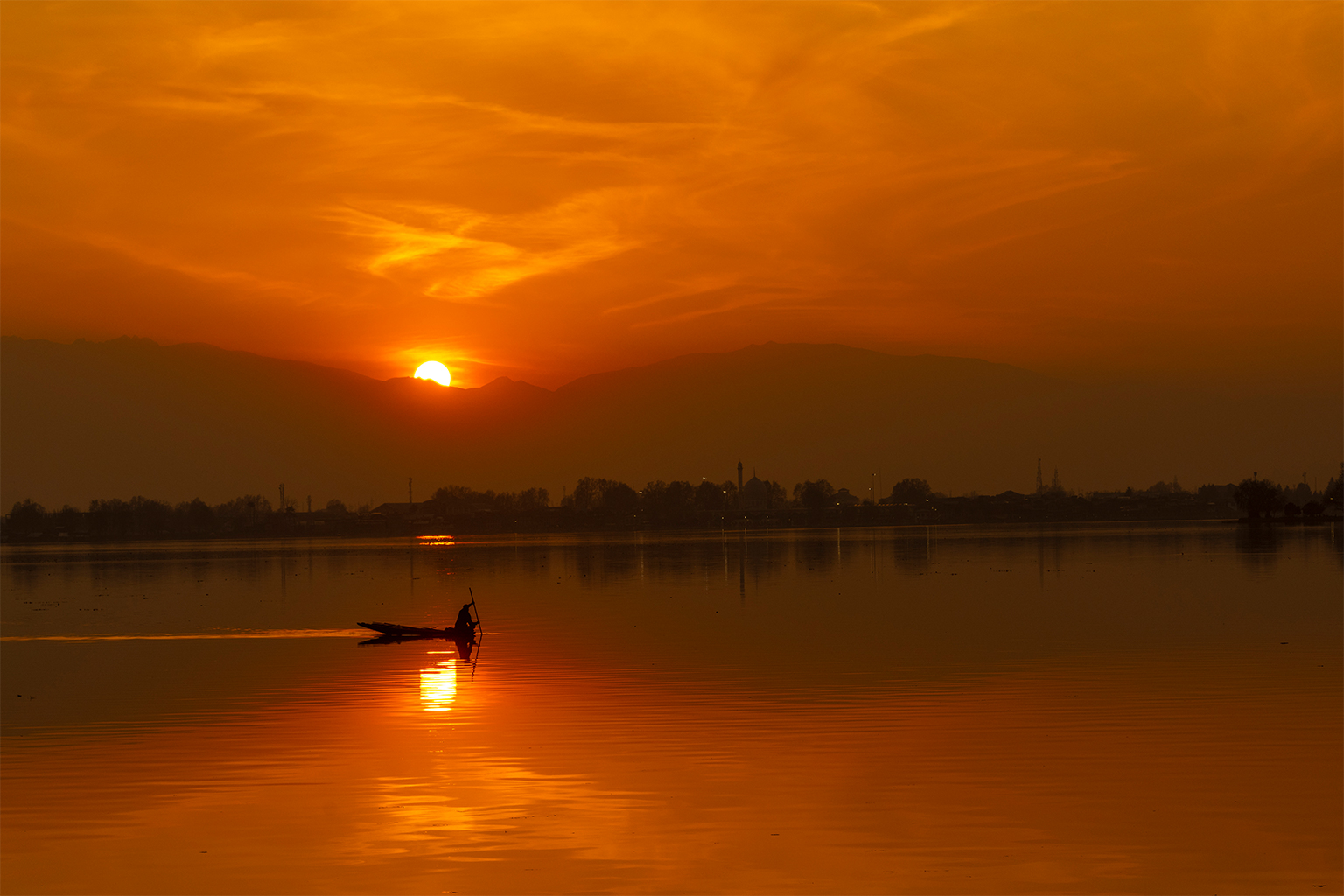 Een visser roeit zijn shikara, of traditionele houten boot, op weg naar huis tijdens zonsondergang bij Dal Lake