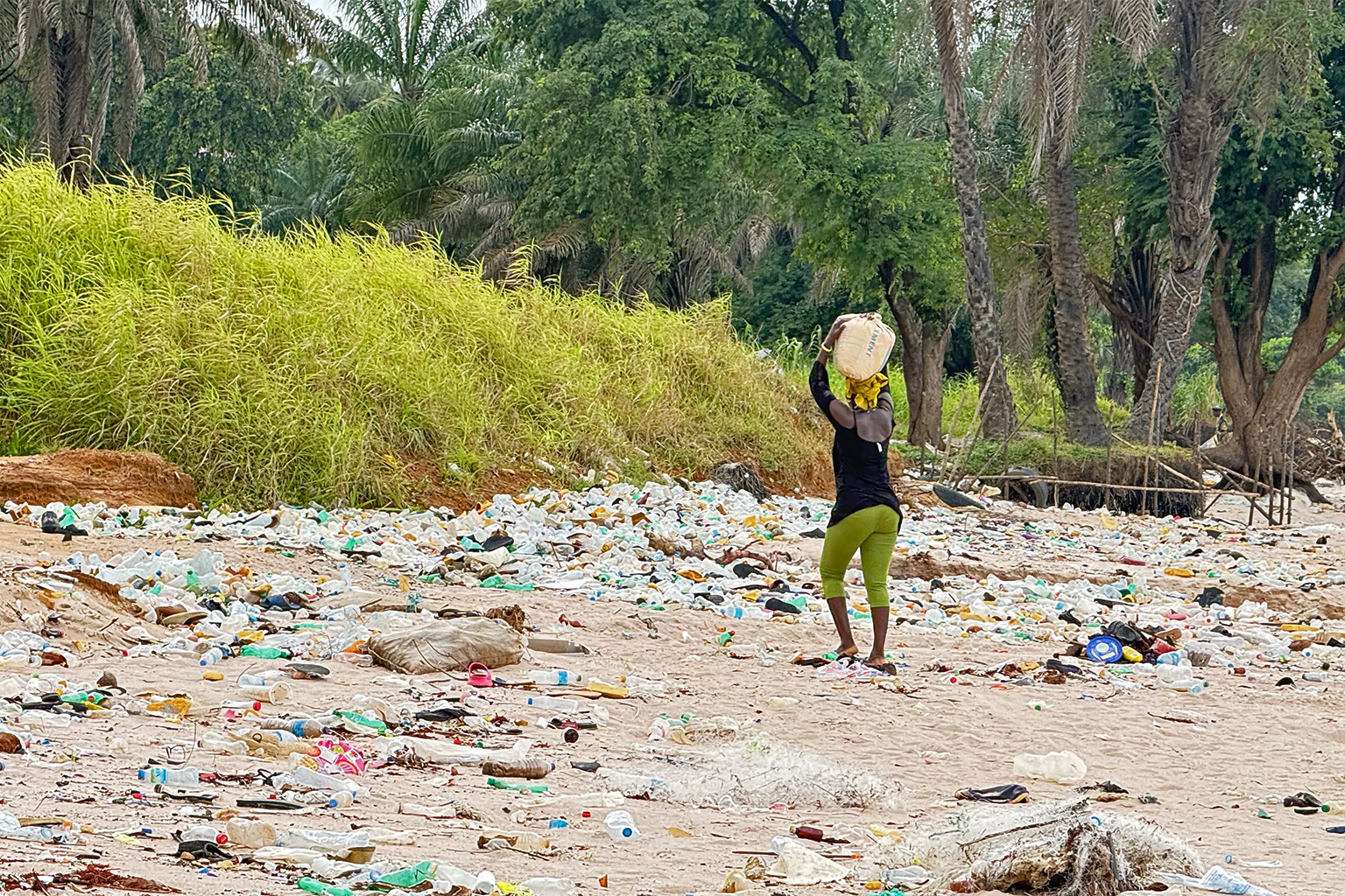 Een vrouw draagt ​​een geladen zak zand op haar hoofd terwijl ze wegloopt van het strand in Sierra Leone. Afbeelding door Patricia Sia Ngevao.