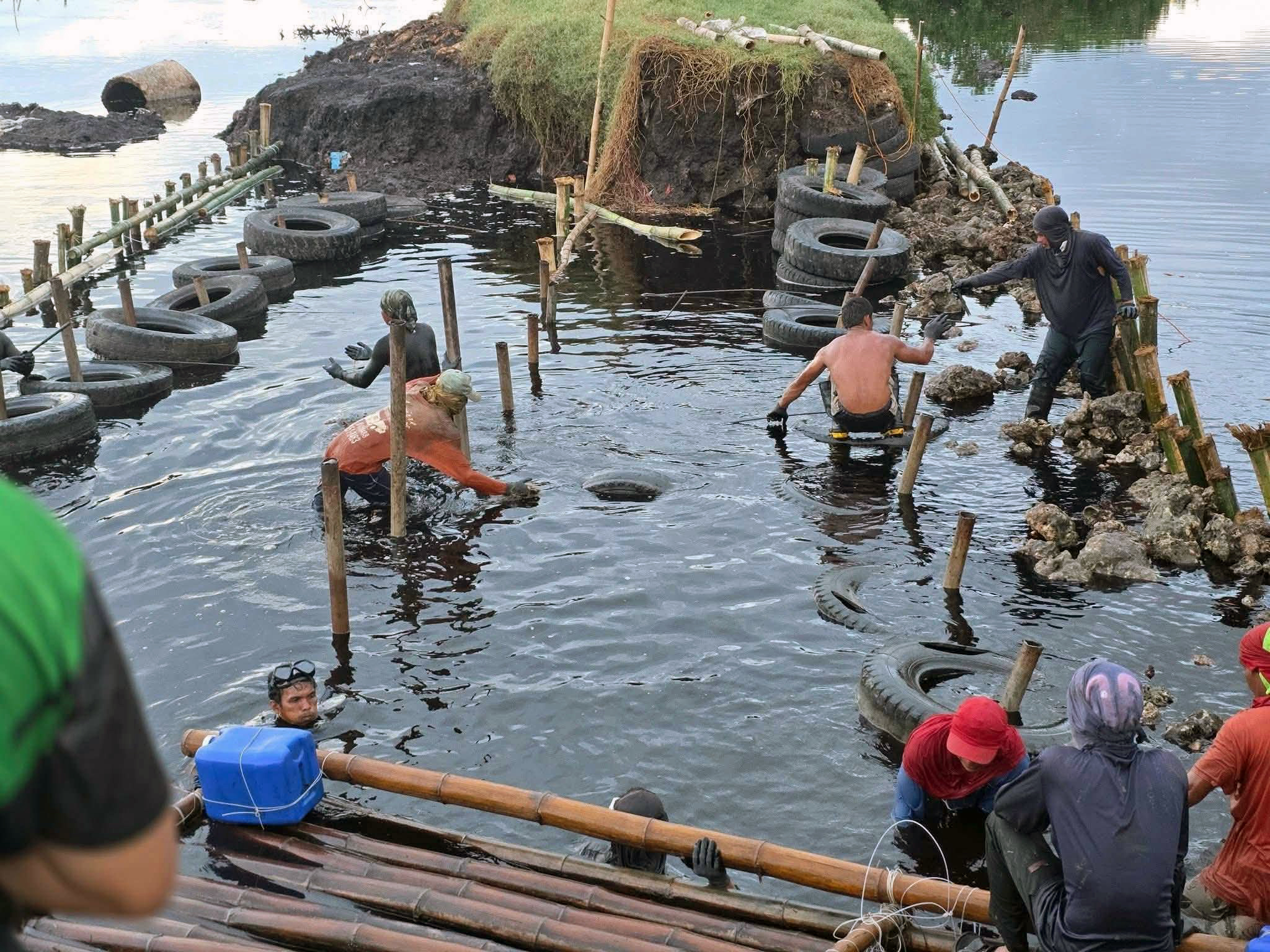 Werknemers bouwen op 28 oktober 2026 een barrière van banden, bamboe en steen in de donkere wateren van Bais Bay in de Filippijnse provincie Negros Oriental, dagen nadat ethanolafvalwater in de baai stroomde. Afbeelding met dank aan MarGale Bancairen.